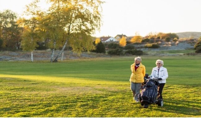 Two women walking a golf fairway with a push cart on an autumn morning