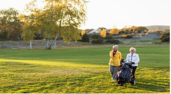 Two women walking a golf fairway with a push cart on an autumn morning